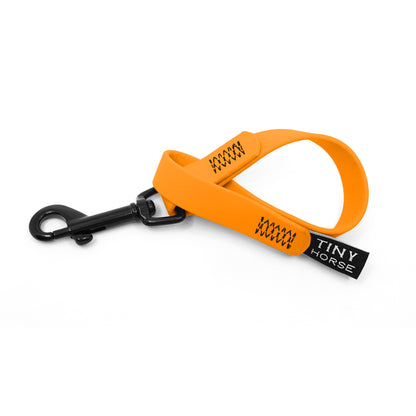 A pastel orange keeper in bio thane with a black trigger clip on a white background.