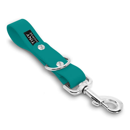 A teal Sidekick Hands free dog walking attachment with silver trigger clip on a white background.